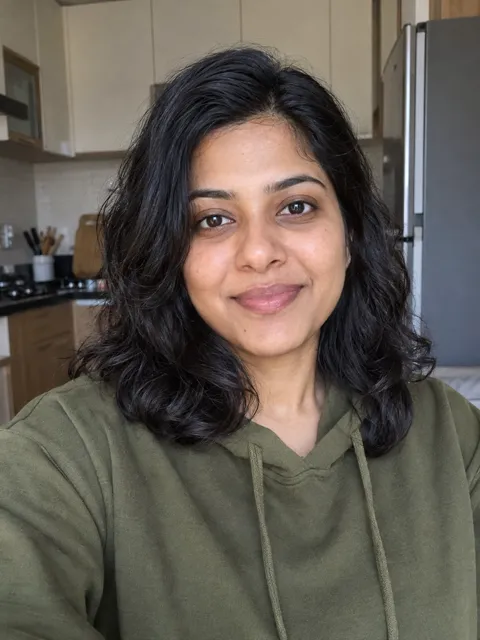 Photo of a South Indian woman, early 30s, shoulder-length wavy black hair, olive green hoodie
