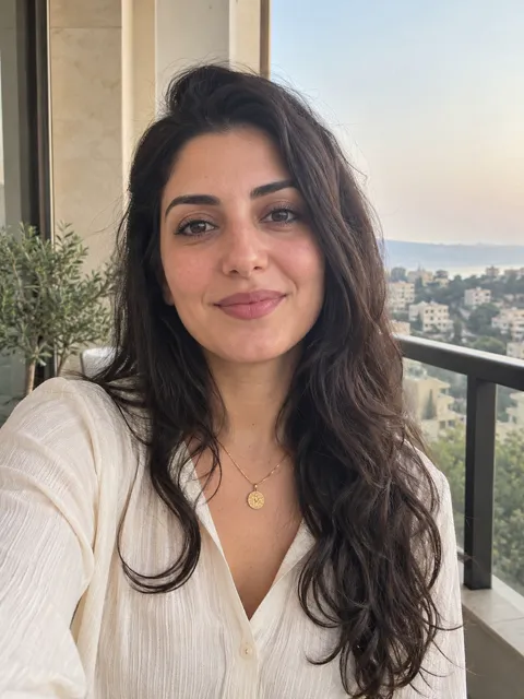 Photo of a Lebanese woman, early 30s, long dark wavy hair, gold necklace, cream blouse